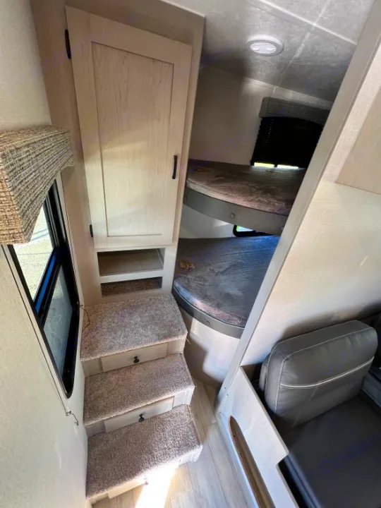 Explore this RV rental's compact interior: bunk bed, cabinet, and carpeted stairs to a cushioned upper bed/lounge.. Coachmen Clipper 262 BH C 2023