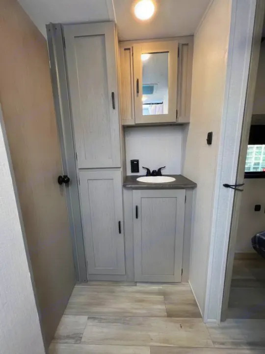 Modern RV rental vanity features light grey cabinets, a mirror, and a sink. Includes ample storage and wood-look flooring.. Coachmen Clipper 262 BH C 2023