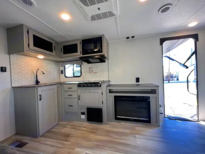 Modern RV rental kitchen & living space. Features a stove, microwave, sink, fireplace, and light wood flooring for comfort.. Coachmen Clipper 262 BH C 2023