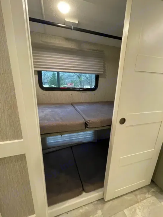RV rental interior: A bright, comfortable bunk/bed area with a window (showing 'EXIT' sticker), light, and white cabinets.. Other Other 2021