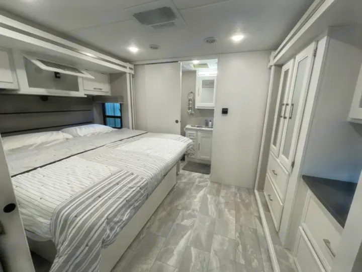 Modern RV rental interior: elevated bed, white cabinetry, compact bath area. Clean & efficient living space.. Other Other 2021