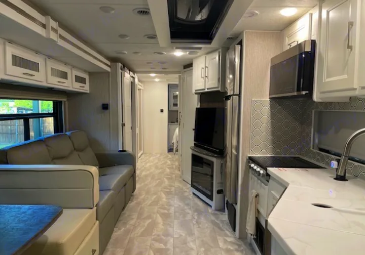 A bright, modern RV rental interior showcasing a kitchen with white cabinets, living area sofa, and light flooring.. Other Other 2021