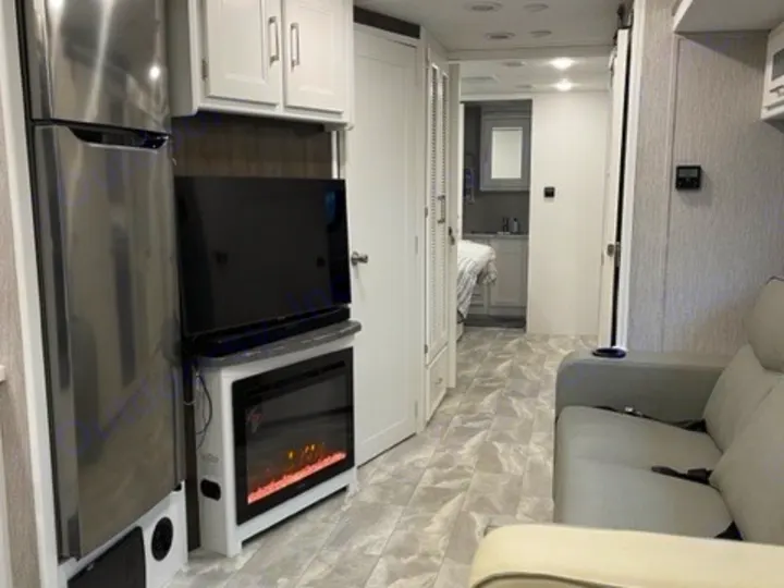 RV rental: Modern interior featuring a stainless fridge, TV, electric fireplace, sofa, and a hallway leading to the bedroom.. Other Other 2021