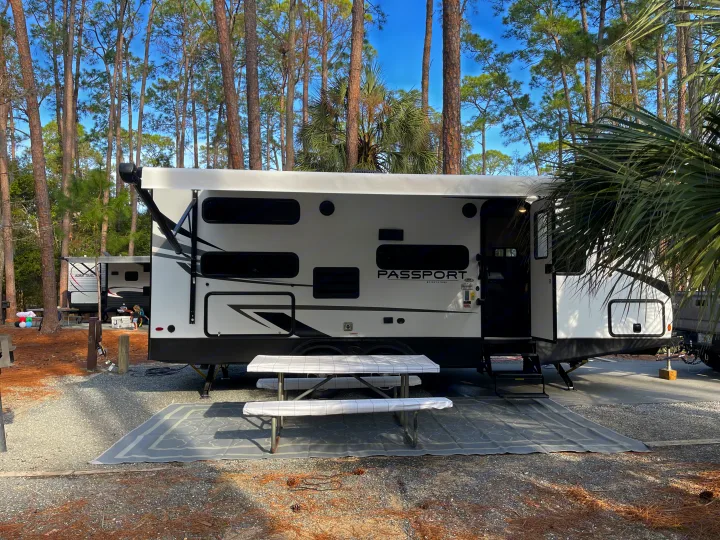 Enjoy this Keystone Passport RV rental at a serene campsite, complete with a picnic table, mat, and surrounding tall trees.. Keystone RV Passport SL 2022