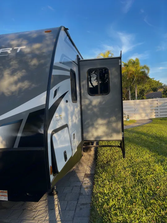 RV rental: A grey travel trailer with its rear ramp door open, parked on a paver patio in a sunny backyard.. Keystone RV Passport SL 2022