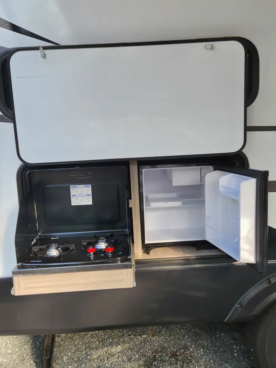This RV rental features an open outdoor kitchen with a mini-fridge and two-burner stove, perfect for camping.. Keystone RV Passport SL 2022