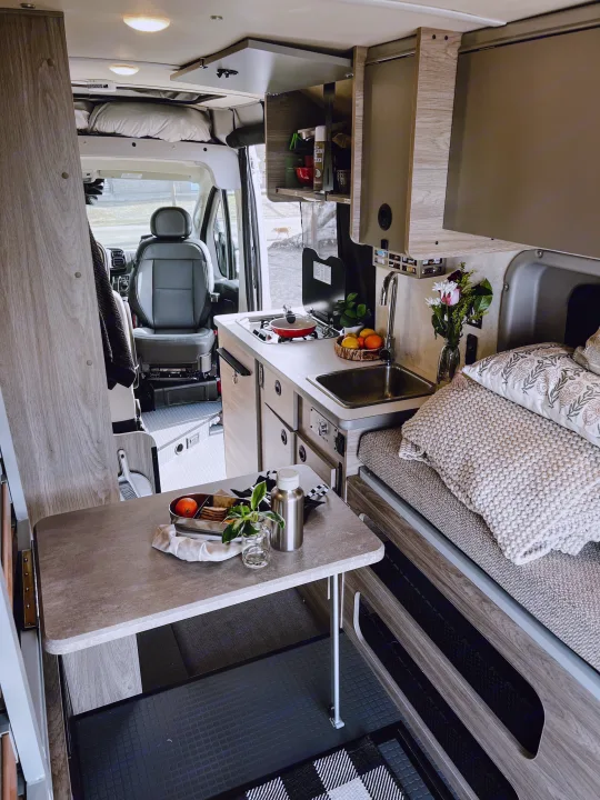 Inside a stylish RV rental, showcasing a fully equipped compact kitchen, dining area, and comfortable sleeping space.. Winnebago Solis 59PX 2023