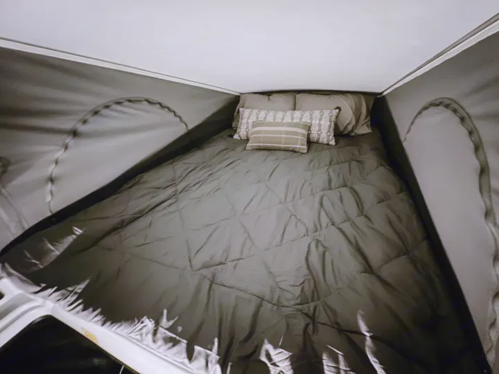 Cozy RV rental pop-top bed, perfect for travel. Dark comforter and pillows on a comfortable mattress inside a camper.. Winnebago Solis 59PX 2023