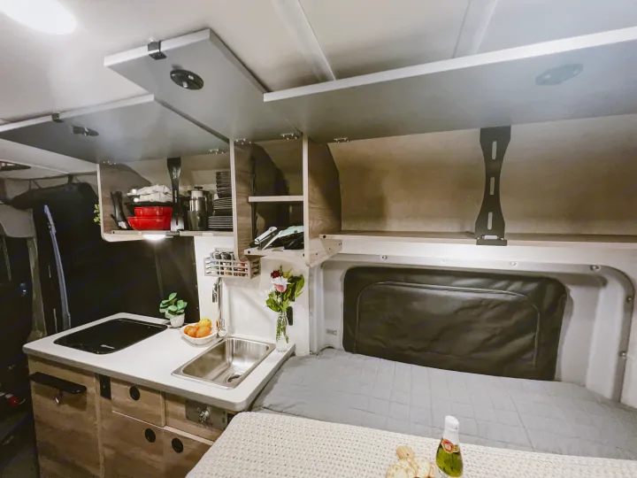RV rental camper van interior featuring a compact kitchen, open cabinets, and comfy bed for travel.. Winnebago Solis 59PX 2023