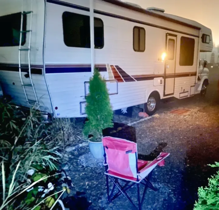RV rental parked for the night, with an outdoor chair and potted tree next to the motorhome.. Ford Econoline 1988