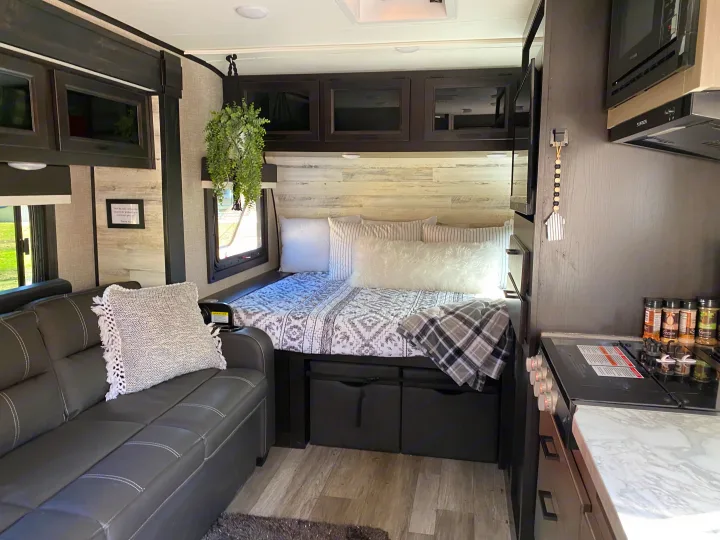 Cozy RV rental interior: bed with patterned bedding, couch, dark cabinets, kitchen area, and wood-look flooring.. Jayco Jay Feather Micro 2022