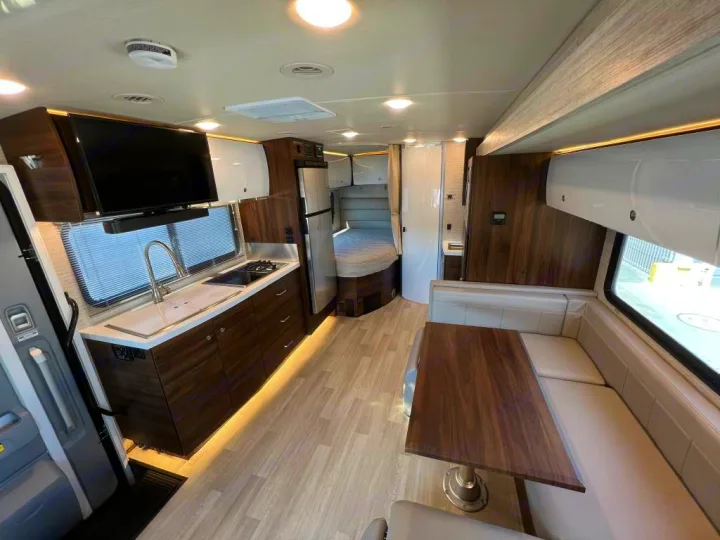 Bright RV rental interior: Well-equipped kitchen, U-shaped dinette, and bed area. Enjoy mobile comfort on your travels.. Winnebago Navion 2021