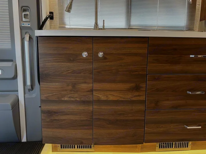 Modern RV rental kitchen with dark wood cabinets, sink, and entryway details. Ready for your next adventure.. Winnebago Navion 2021