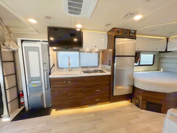 Explore this modern RV rental interior: a sleek kitchen with dark wood cabinetry & stainless fridge, plus a cozy bed area.. Winnebago View 2022