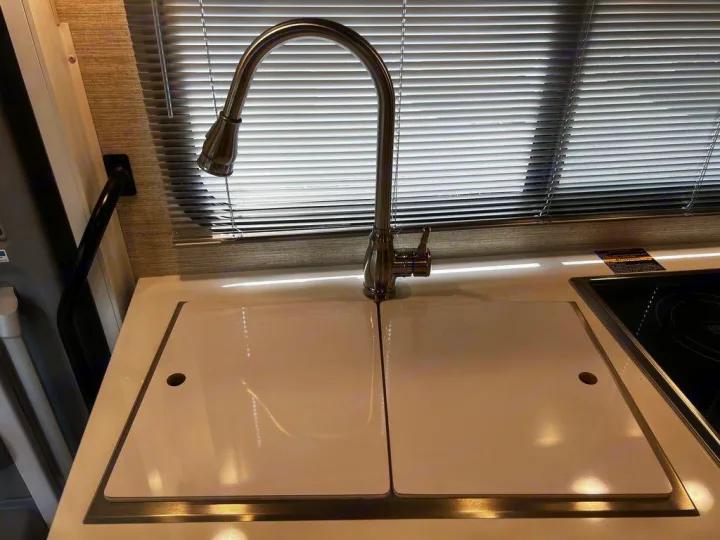 RV rental kitchen counter features a brushed metal faucet, two white sink covers, and a black induction cooktop.. Winnebago View 2022