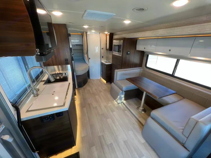 Modern RV rental interior showcasing a full kitchen, comfortable dining booth, and living space with sleek finishes.. Winnebago View 2023