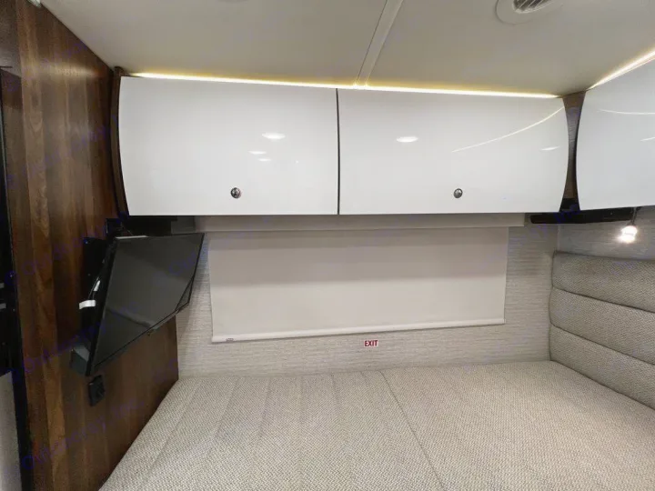 RV rental bedroom features a comfy bed, mounted TV, sleek overhead cabinets, and a privacy blind.. Winnebago View 2023