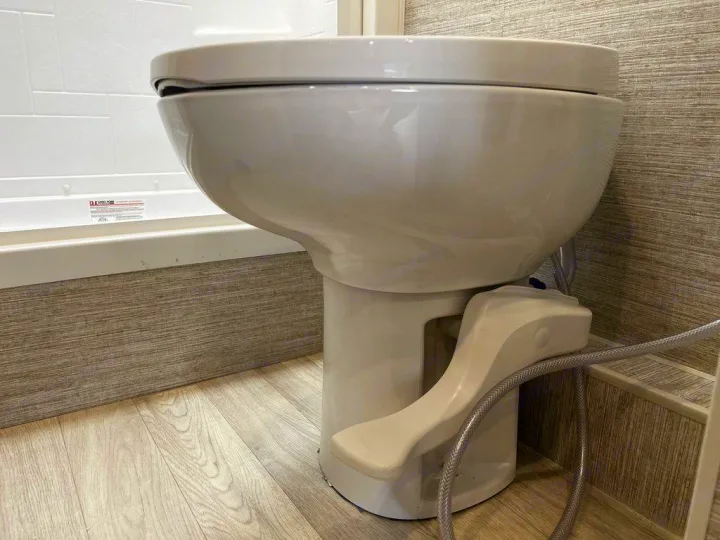 A compact, foot-pedal RV toilet with an attached bidet sprayer in a small bathroom, common in an rv rental.. Winnebago View 2023