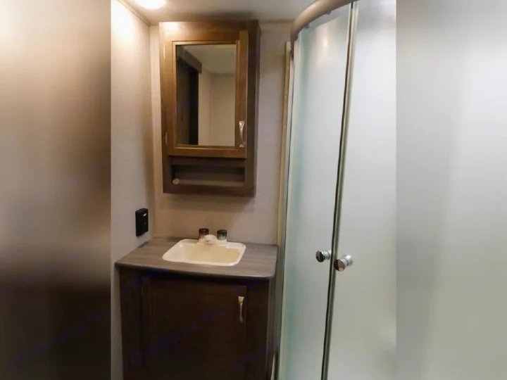 Compact RV rental bathroom featuring a vanity with a sink, medicine cabinet, and a frosted glass shower.. Dutchmen Coleman Light 2018