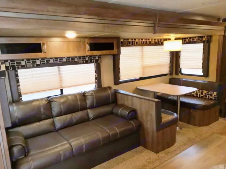 Inside this rv rental: a cozy living area with a dark sofa and dinette seating. Ideal for comfortable travel.. Dutchmen Coleman Light 2018