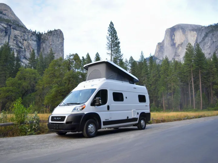 Explore Yosemite! This white RV rental camper van with a pop-top is parked on a road amidst Half Dome and pine trees.. Winnebago Solis 2021