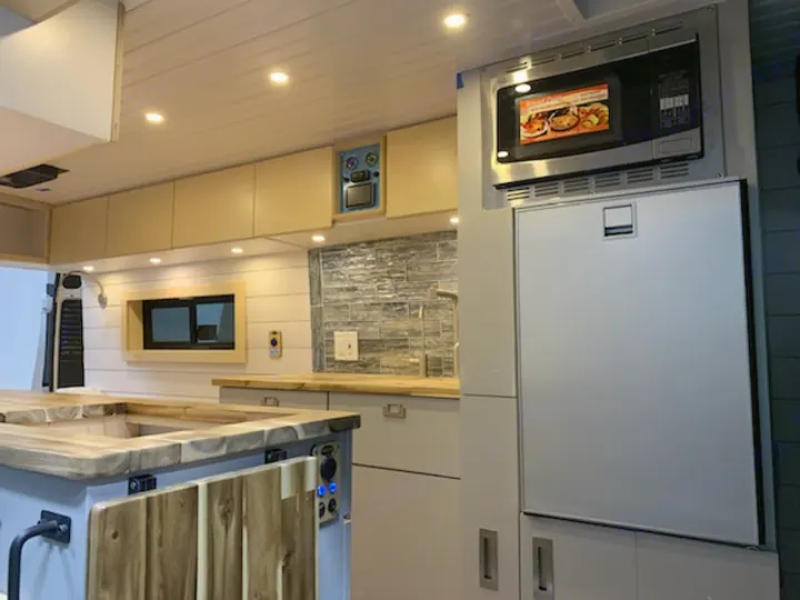 Inside a premium rv rental: a full kitchen with microwave, large fridge, custom counters, and storage.. Ram 3500 Extended 2021