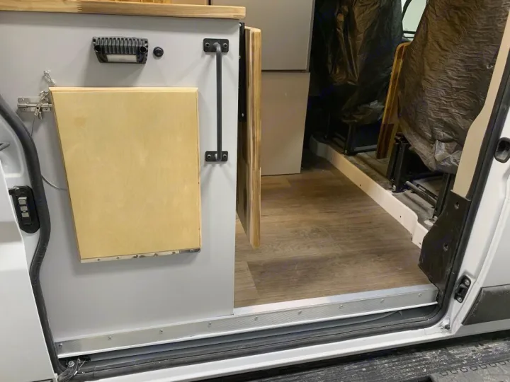 RV rental: customized camper van interior with a light wood folding table, laminate floor, and open sliding door.. Ram 3500 Extended 2021
