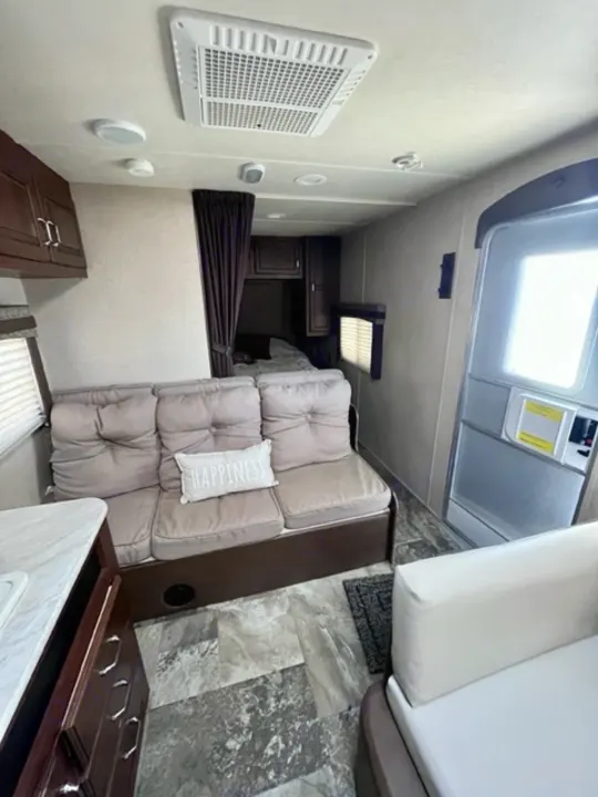 Inside an RV rental: Compact living space with a cushioned sofa, forward bedroom behind a curtain, entry door, and AC.. Jayco Jay Flight 2015