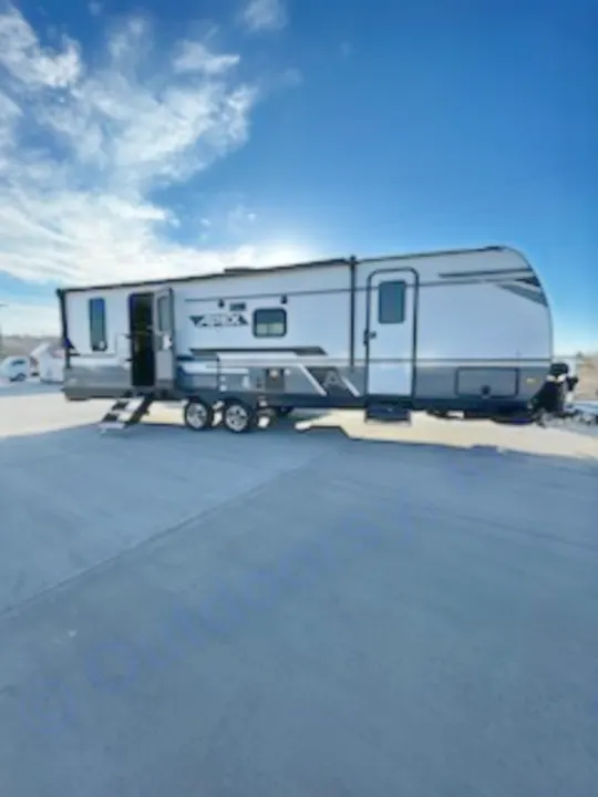 A sleek white and gray travel trailer is parked, ideal for RV rental adventures. Steps down, door open under a blue sky.. Coachmen 266 BHS 2023