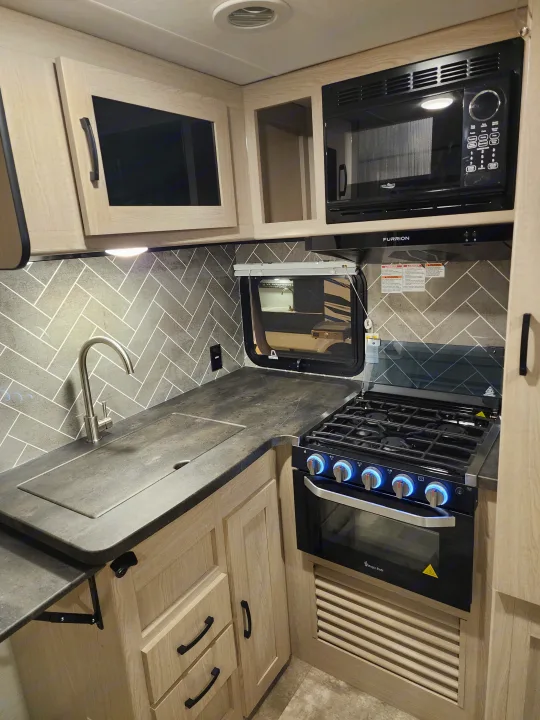 RV rental kitchen: High Pointe microwave, Magic Chef stove, sink, modern light wood cabinets & herringbone floor.. Coachmen 266 BHS 2023