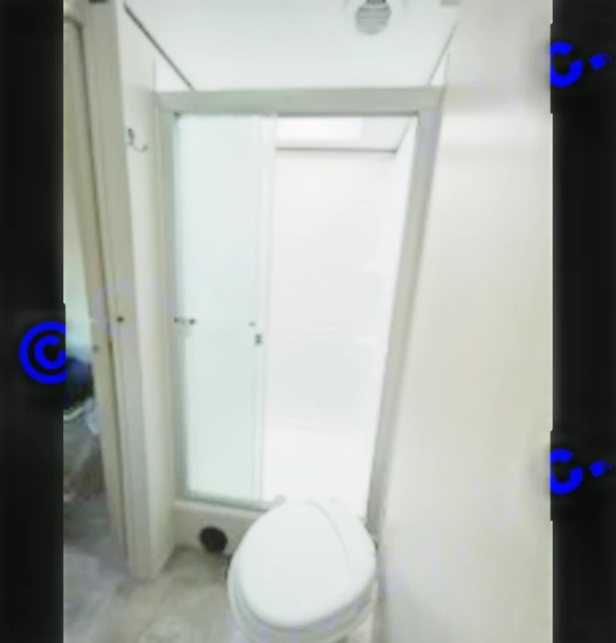 Inside an RV rental: a compact bathroom with a white toilet and a shower stall featuring a sliding frosted door and white tiles.. Coachmen 266 BHS 2023