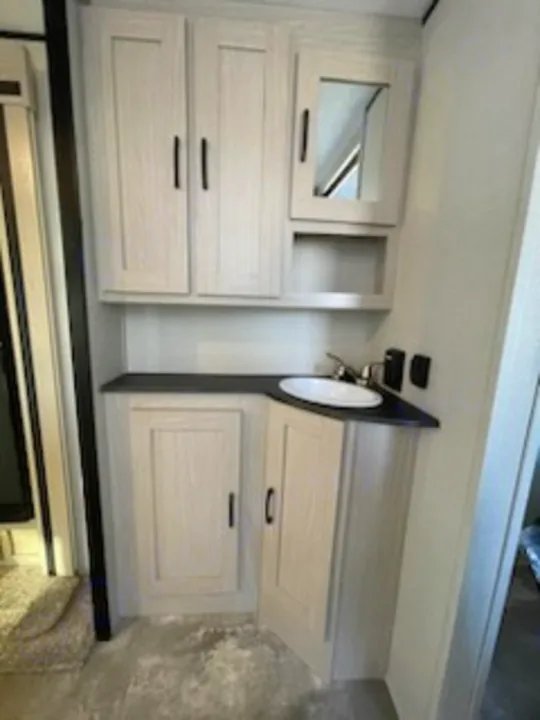 RV rental bathroom vanity with light-toned cabinets, sink, and mirror. Ideal for convenience and storage in your RV adventure.. Coachmen 266 BHS 2023