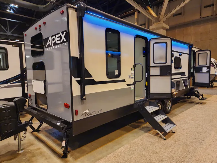 Apex Ultralite travel trailer, an excellent RV rental option, with bright blue LED lighting, open door, and stairs.. Coachmen 266 BHS 2023