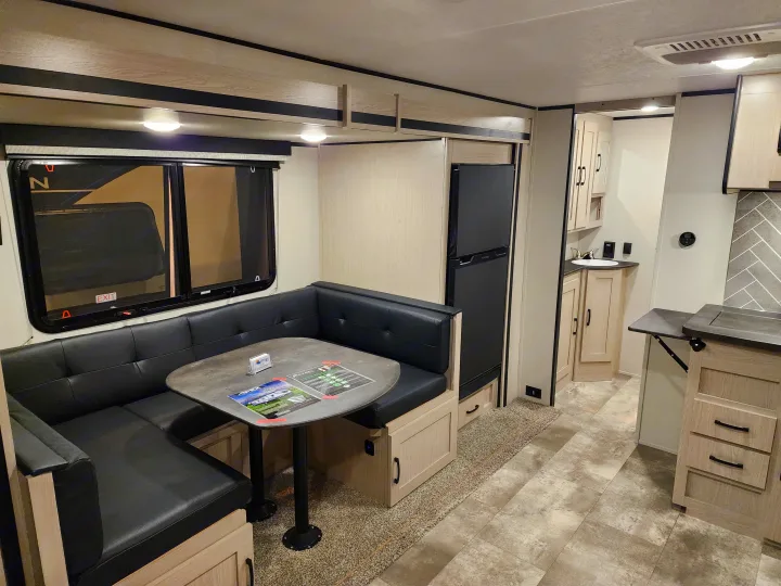 This RV rental interior features a U-shaped dinette with black cushions, a kitchen area, and a black refrigerator.. Coachmen 266 BHS 2023