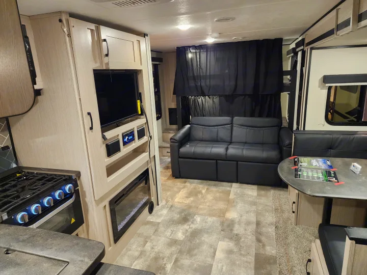 Spacious RV rental interior with light-colored kitchen (stove, oven), living area (sofa, TV, fireplace), and dining table.. Coachmen 266 BHS 2023