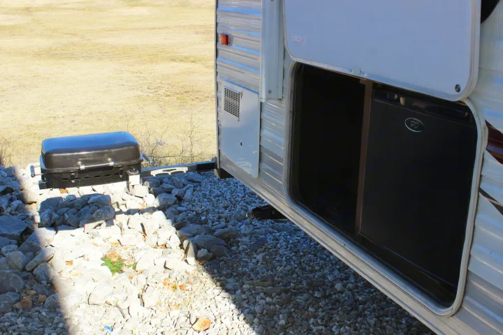 RV rental exterior with open storage holding a mini-fridge, next to a portable grill on rocks.. Jayco Jay Flight 2015