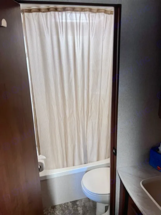 Inside an RV rental bathroom: a shower/tub with striped curtain, toilet, and partial view of the sink vanity.. Jayco Jay Flight 2015