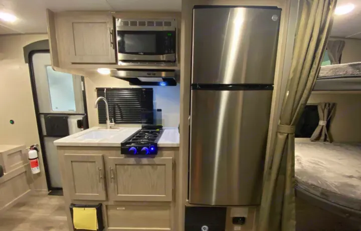 This RV rental features a compact kitchen with a fridge, microwave, gas stove, sink, and bunk beds.. Forest River Coachmen Catalina Summit 2022