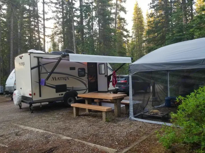 RV rental parked at a tranquil forest campsite, featuring an extended awning, picnic table, and screened tent for outdoor living.. Gulf Stream Other 2018