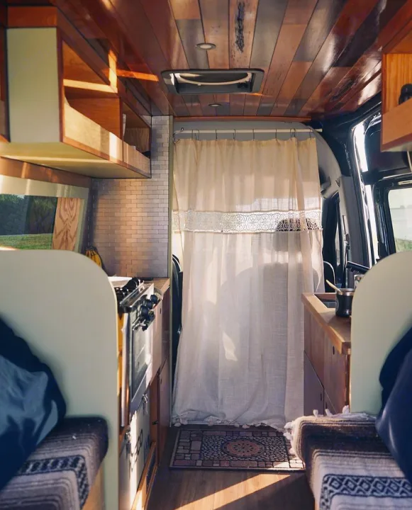 Inside a cozy rv rental, this camper van features a warm wooden ceiling, compact kitchen, and privacy curtain separating the cab.. Mercedes Sprinter 2013