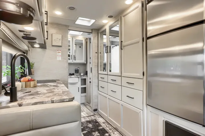 Spacious RV rental interior featuring a modern kitchen, stainless steel fridge, and sleek storage leading to the bathroom.. Thor Vegas 2022