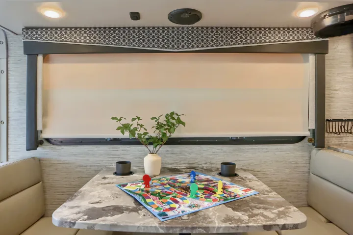 Inviting RV rental dinette with a board game (Candy Land), plant, and cups on a marble table. Window shade.. Thor Vegas 2022