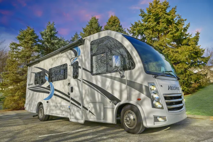 Experience an RV rental! This Vegas motorhome is ready for adventure, parked among evergreens under a vibrant sunset sky.. Thor Vegas 2022