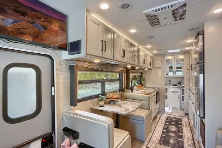 Bright, modern RV rental interior featuring a well-equipped kitchen, comfortable dinette, TV, and ample storage for travel.. Thor Vegas 2022