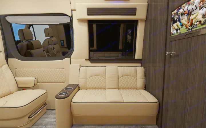 Plush RV rental interior with cream leather seats, diamond stitching, TV, dark wood accents, and a large window.. Ultimate Toys Ultimate Cruiser 2022
