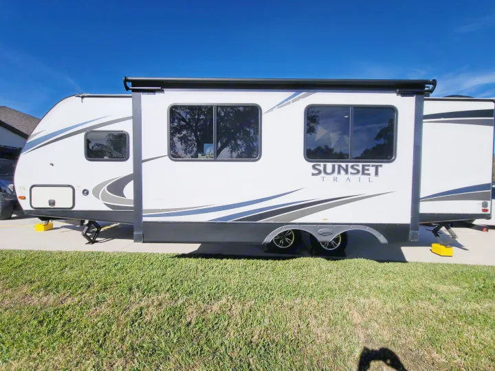 White travel trailer RV rental, parked with slide-out extended. Features awning and leveling jacks, ready for adventure.. Crossroads RV Sunset Trail Super Lite 2018