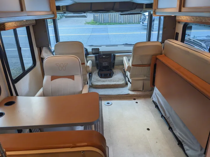 Explore a comfortable RV rental interior: front captain's chairs, dining booth, and convertible sofa for travel.. Winnebago Brave 2015