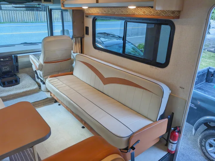 Spacious rv rental interior showcasing a neutral-toned sofa, comfortable swivel driver's seat, and bright windows.. Winnebago Brave 2015