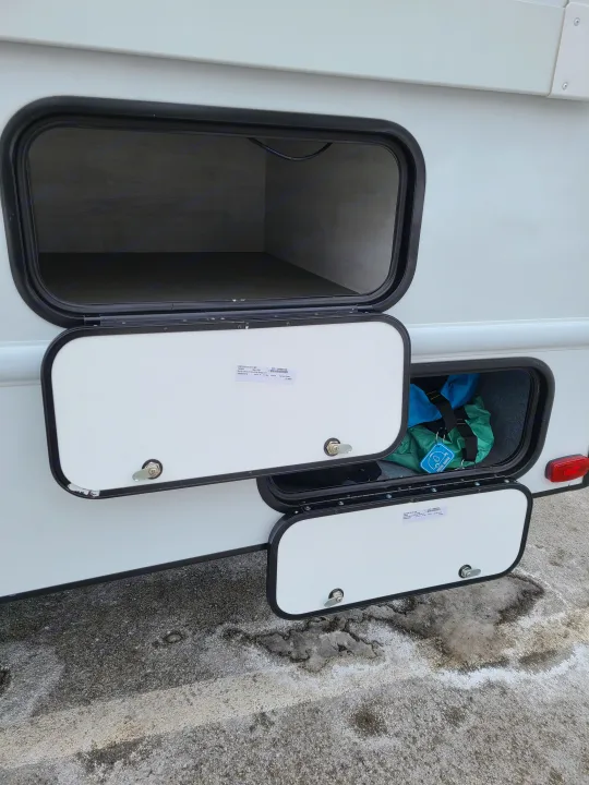 RV rental with multiple open storage compartments. Large upper bay is empty, lower holds 'Fresh Water' travel gear.. East to West Entrada 2023
