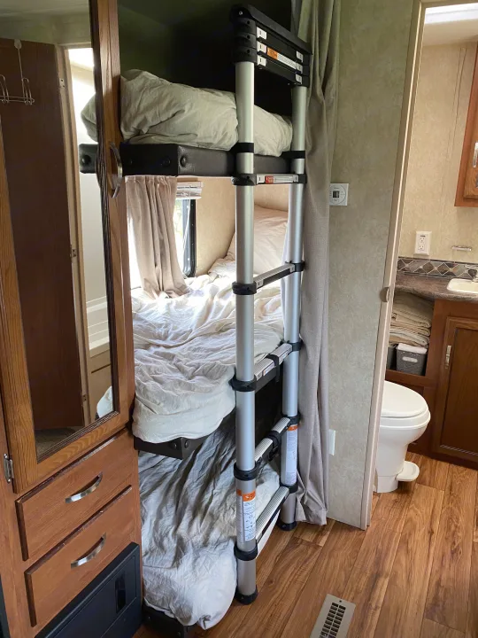 Cozy RV rental interior featuring comfortable bunk beds with a ladder, and a compact bathroom area. Ideal for family adventures.. Forest River Salem 2015
